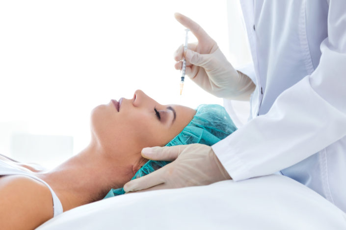 Beautiful young woman getting botox cosmetic injection in her fa