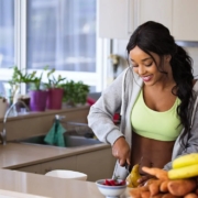 Mujer en ropa de deporte partiendo una pera junto a montaña de fruta