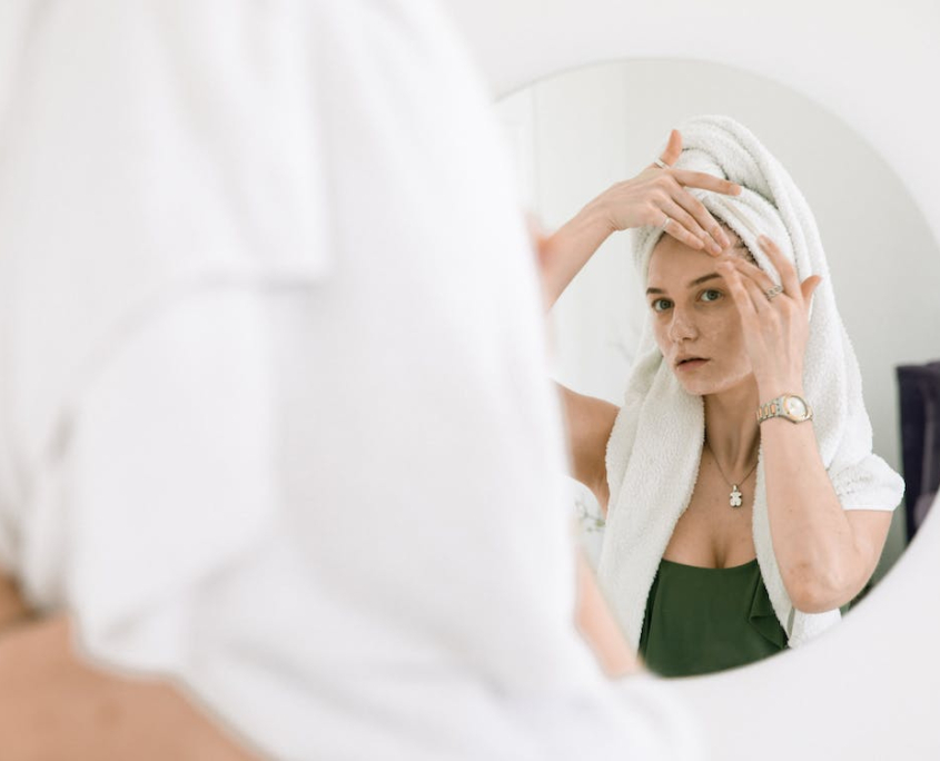 Mujer con toalla mirándose al espejo y tocándose la cara tras lifting facial