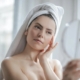 Una mujer con toalla en la cabeza mirándose al espejo porque se siente guapa tras lifting facial