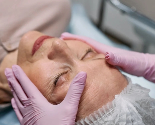 mesoterapia-facial-que-es Manos con guantes de látex rosa tocando rostro de mujer sometiéndose a mesoterapia facial